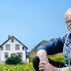 Oddgeir Bruaset sit føre barndomsheimen med eit kamera som peikar på seg.