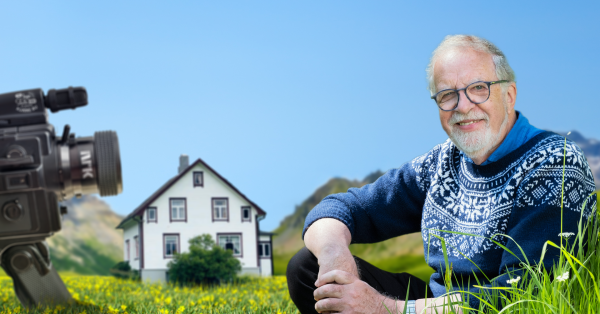Oddgeir Bruaset sit føre barndomsheimen med eit kamera som peikar på seg.